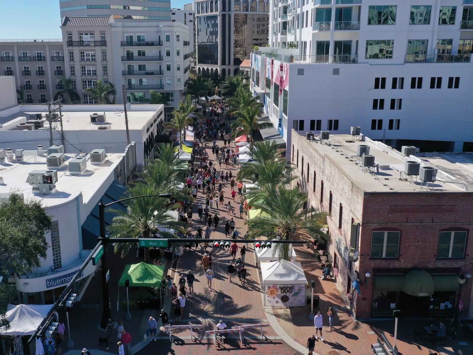 The Saturday farmers market filling Main Street in downtown Sarasota, white vendor tents and crowds between the storefronts and palms
