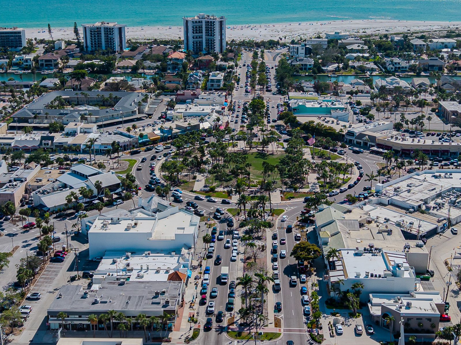 Aerial view of St. Armands Circle, the palm-lined shopping and dining roundabout on St. Armands Key, with Lido Beach and the Gulf of Mexico beyond