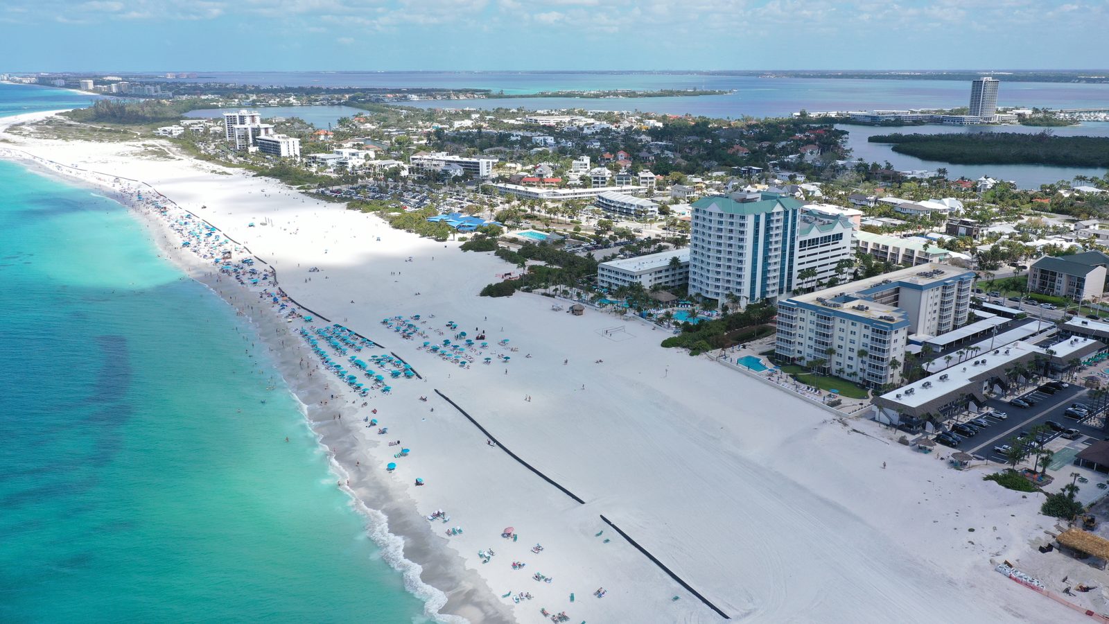 Aerial view of the wide white sand of Lido Beach, Gulf-front condominiums, and the bayou and bay behind the island